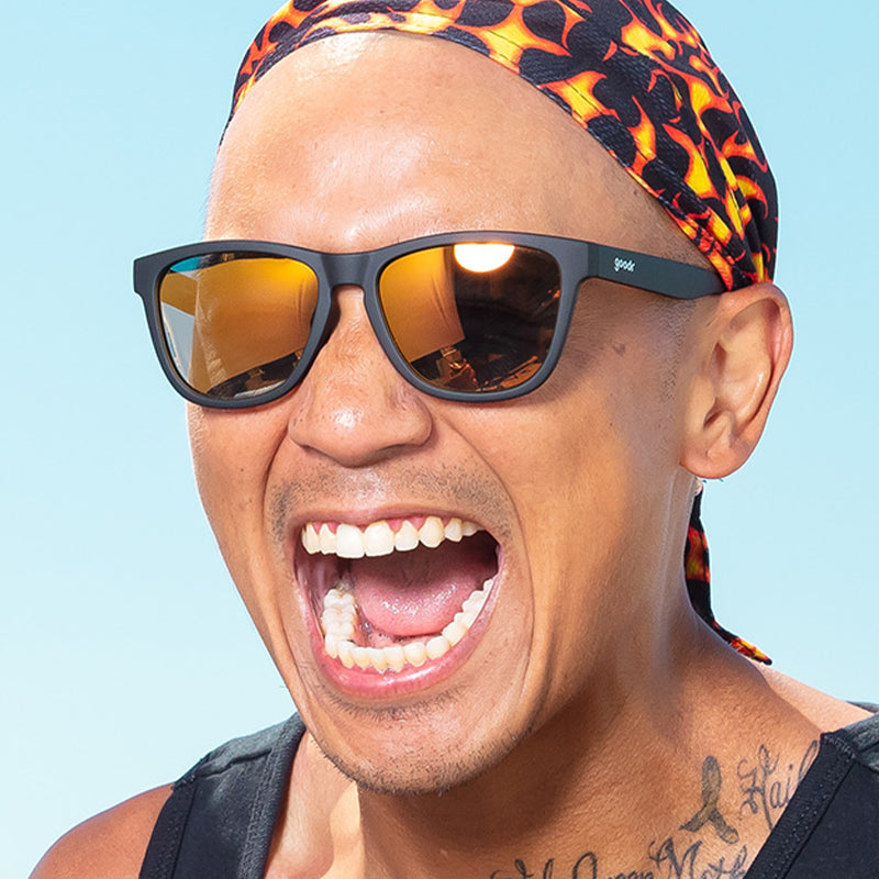 Un hombre con un durag en llamas y gafas de sol negras con cristales reflectantes ámbar grita alegremente.