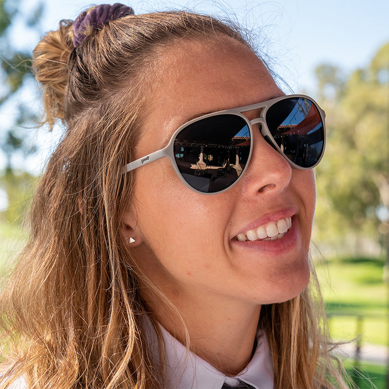 Una mujer sonriente con camisa de cuello en un club de golf lleva gafas de sol de aviador grises con cristales no reflectantes.