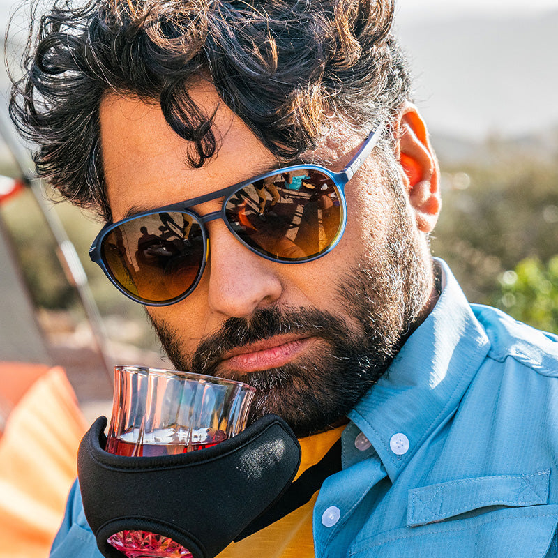 Un hombre barbudo con gafas de sol azules de aviador aspira whisky de un artilugio que podría verse en un catálogo de Skymall.
