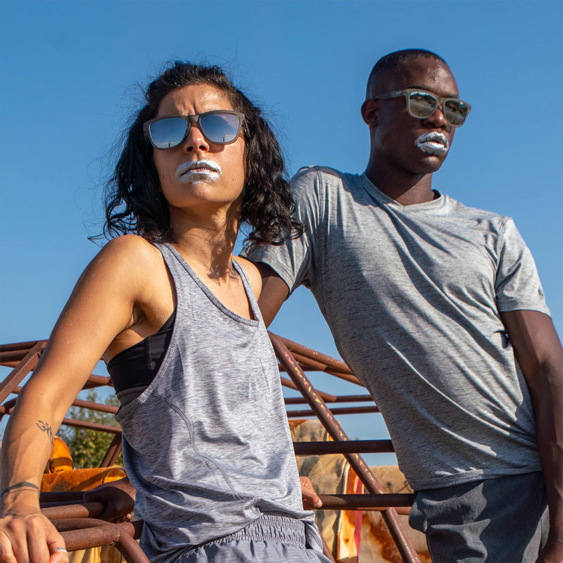 Un hombre y una mujer con gafas de sol grises con cristales grises y pintura plateada en la boca miran a lo lejos con fiereza.