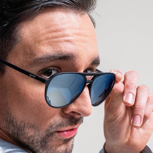 Un hombre mira por encima del hombro con unas gafas de sol de aviador negras y cromadas deslizadas por la nariz.