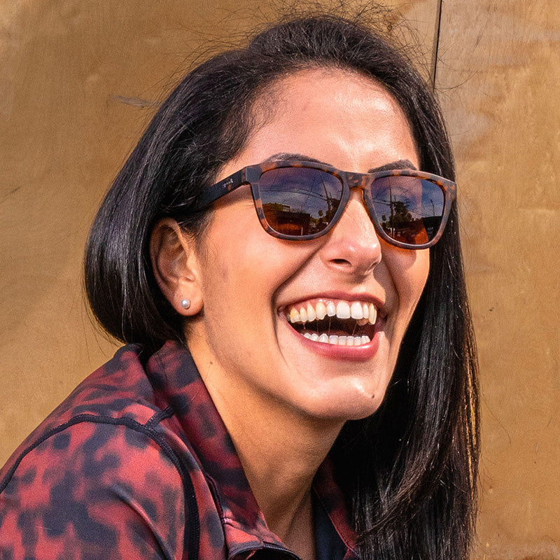 Una mujer morena con gafas de sol de carey con cristales marrones ríe bajo el sol.