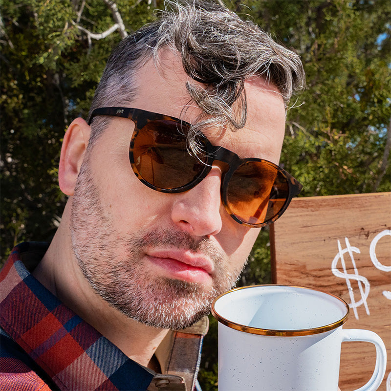 Un camarero hipster mira con displicencia al frente con unas gafas de sol de carey marrones con cristales antirreflejantes marrones.