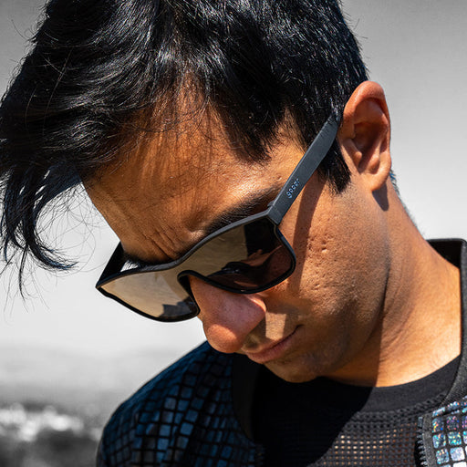 Un hombre con gafas de sol negras planas de una sola lente mira hacia un lado, decidido.
